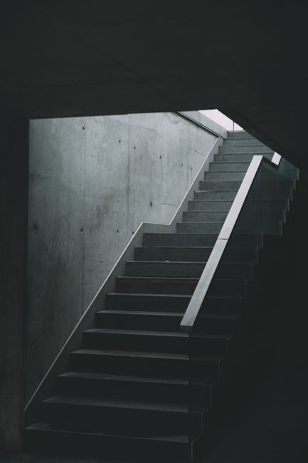 A set of industrial metal stairs with black treads and yellow safety edges, leading upwards in an indoor environment, possibly a warehouse or factory. The stairs have handrails on both sides painted in bright yellow, providing support for users. The background shows structural steel beams, pipes, and other industrial fixtures, indicating a high-bay storage or manufacturing setting. A sign affixed to the middle of the stairs reads 'PLEASE KEEP LEFT,' suggesting a safety or directional instruction. The lighting appears to be artificial, casting a consistent illumination across the scene. The overall environment appears utilitarian with a focus on functionality and safety, aligning with a setting where waste removal or site clearance activities could take place, especially in reference to independent or private disposal methods handled by companies like Rubbish Clearance Highbury.